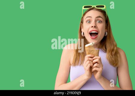 Jeune femme surprise avec de la crème glacée à la vanille mordue dans une tasse à gaufres sur fond vert Banque D'Images