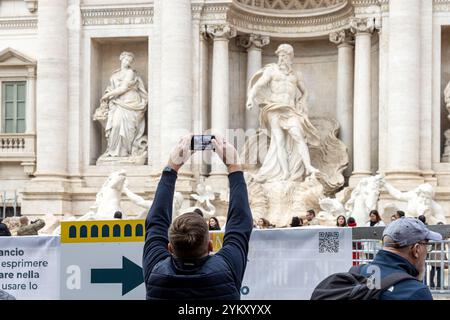 Rome, Italie - 14 novembre 2024 : un visiteur photographie la fontaine de Trevi au-dessus des barrières de construction pendant les rénovations pour Jubilé Banque D'Images