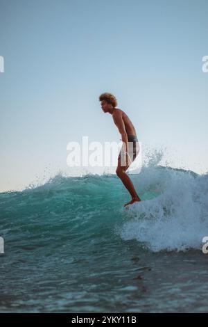 Un homme surfe sur une vague dans l'océan. Il porte un short et a les pieds sur la planche de surf Banque D'Images