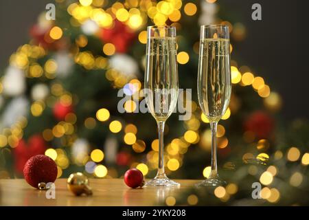 Champagne en verres et ornements festifs sur table en bois contre les lumières de Noël floues, espace pour le texte. Effet bokeh Banque D'Images