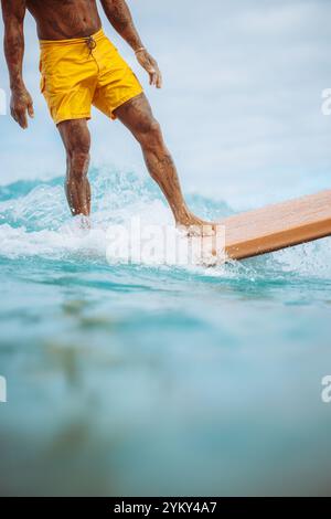 Un homme en short jaune surfe sur une planche de surf. La planche de surf est orange. L'eau est bleue Banque D'Images