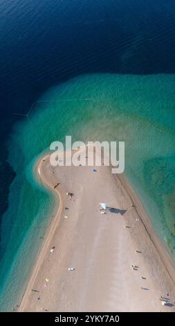 À Brac Island, les baigneurs profitent d'une journée sereine sur la plage de sable, embrassée par des eaux turquoises cristallines. Le paysage vibrant invite à la détente Banque D'Images