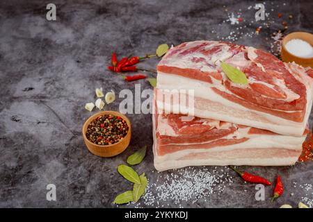 Ventre de porc fraîchement coupé avec des épices et des herbes sur fond texturé prêt pour la préparation culinaire Banque D'Images