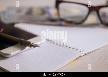 Cahier avec des pages vierges se trouve ouvert à côté du stylo plume smartphone plusieurs factures sont à proximité, suggérant un environnement organisé pour la planification de la prise de notes. Banque D'Images
