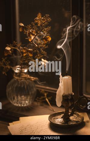 un vase en verre contenant des fleurs d'hortensia séchées et une bougie éteinte avec une belle fumée, créant une scène automnale confortable sur un rebord de fenêtre Banque D'Images