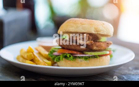 burger de rue avec escalope de poisson et légumes et frites sur assiette blanche. Banque D'Images