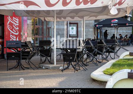 Biélorussie, Minsk - 29 octobre 2023 : sous un grand parapluie, il y a des tables et des chaises disposées, tandis qu'un distributeur automatique de coca cola se dresse prominentl Banque D'Images
