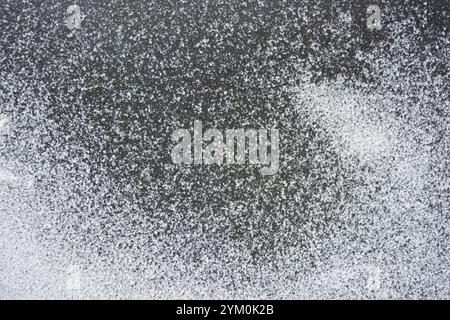 Beau fond en caoutchouc noir avec de petits grains de neige blanche. Le tapis en caoutchouc noir est recouvert d'une fine couche de neige blanche. Banque D'Images