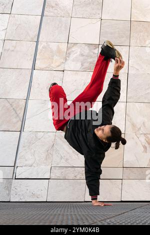 Un jeune homme en pantalon rouge breakdancing exécutant une poignée sur une grille métallique . Concept d'athlétisme et de compétence, comme l'homme est capable d'équilibrer dans un U. Banque D'Images