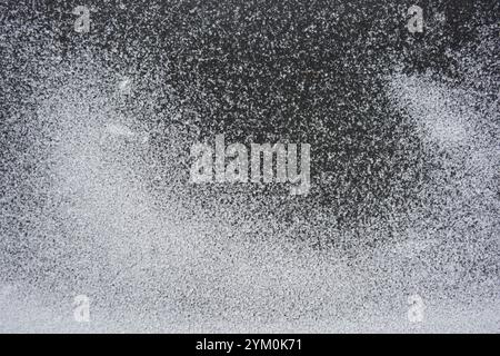 Beau fond en caoutchouc noir avec de petits grains de neige blanche. Le tapis en caoutchouc noir est recouvert d'une fine couche de neige blanche. Banque D'Images