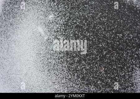Beau fond en caoutchouc noir avec de petits grains de neige blanche. Le tapis en caoutchouc noir est recouvert d'une fine couche de neige blanche. Banque D'Images
