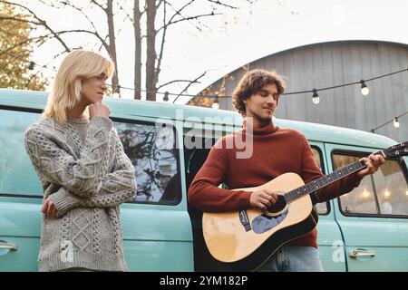 Deux jeunes hommes partagent un moment de joie dans un charmant espace extérieur à l’automne. L'un joue de la guitare tandis que l'autre écoute attentivement, entouré par Banque D'Images