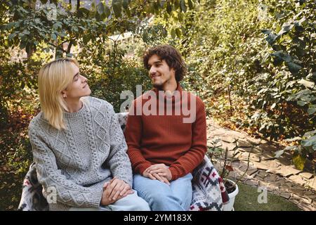 Deux beaux jeunes hommes partagent un moment de rire et de connexion tout en étant assis ensemble dans un jardin luxuriant. Ils sont habillés de chandails confortables, appréciant Banque D'Images