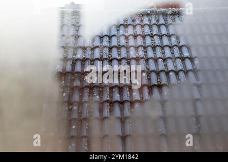 Givre sur un toit vu de l'intérieur d'une maison à travers la condensation sur une fenêtre. Banque D'Images