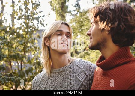 Deux beaux jeunes hommes partagent un regard sincère dans un jardin luxuriant rempli de verdure. Ils rayonnent de joie et de compagnie, profitant d'une belle journée ou Banque D'Images