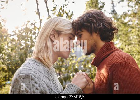 Deux jeunes et attrayants partagent un moment tendre au milieu des feuilles d'automne vibrantes. Leur connexion brille à travers quand ils se tiennent la main et sourient à on Banque D'Images