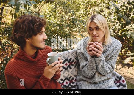 Dans un jardin serein, deux jeunes et belles personnes dégustent des boissons chaudes tout en s'engageant dans une conversation amicale. Banque D'Images