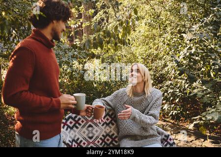 Dans un cadre extérieur serein, deux beaux jeunes partagent une conversation chaleureuse tout en tenant des tasses à vapeur. Banque D'Images