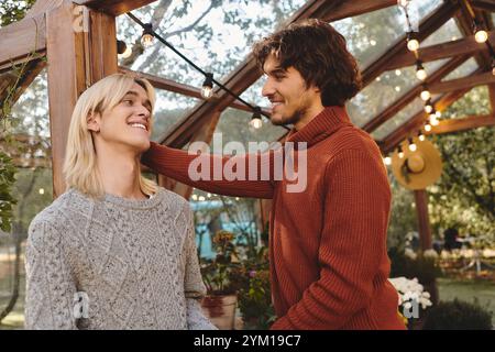 Deux jeunes hommes partagent un moment joyeux dans un jardin vibrant, entouré de verdure luxuriante et d’un décor cosy. Ils s'engagent dans une conversation allégée, emanati Banque D'Images