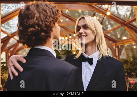 Dans une charmante serre ornée de lumières scintillantes, deux jeunes hommes partagent un moment tendre. Leurs sourires rayonnent de joie, mettant en valeur leur ami de connexion Banque D'Images