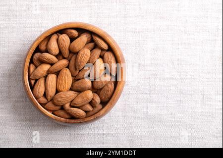 Amandes dans un bol en bois sur tissu de lin, avec un espace vide pour le texte. Noix, graines et fruits de Prunus dulcis, sans coques, bruts, entiers et séchés. Banque D'Images