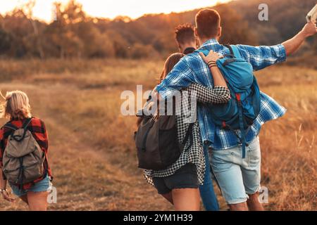 Groupe de quatre amis randonnant à travers la campagne ensemble au coucher du soleil. Banque D'Images