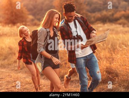 Groupe de quatre amis randonnant à travers la campagne ensemble au coucher du soleil. Banque D'Images