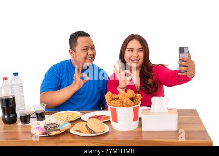 Un couple heureux profite de délicieux fast-food tout en prenant des selfies amusants ensemble Banque D'Images