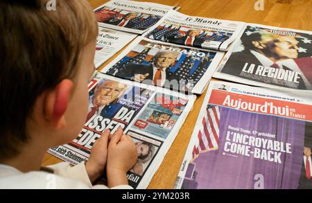 Paris, France - 13 nov. 2024 : un enfant regarde attentivement les premières pages de divers journaux annonçant la victoire électorale de Donald Trump en 2024, soulignant son engagement précoce dans les événements politiques mondiaux Banque D'Images