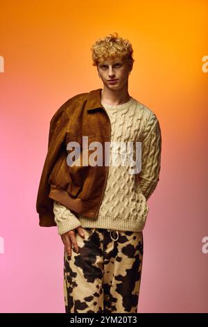 Un homme confiant met en valeur la mode des fêtes avec un pull confortable en maille torsadée et un pantalon à motifs tendance. Il pose sur un fond dégradé vibrant, ble Banque D'Images