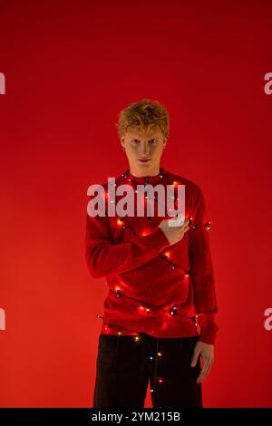 Un jeune homme met en valeur son sens unique du style cette saison des fêtes en portant une tenue rouge festive ornée de lumières de Noël colorées. Banque D'Images