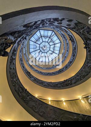 Vue d'en bas d'un escalier en colimaçon orné avec un puits de lumière géométrique au sommet, mettant en valeur des ferronneries complexes. Le Vatican Banque D'Images