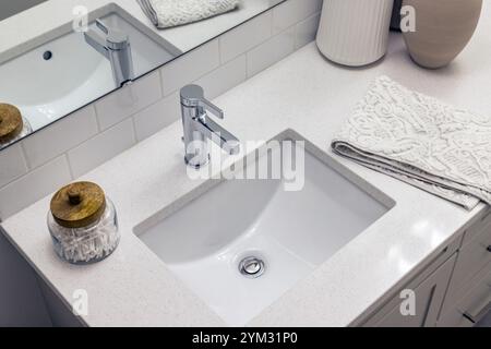 Un lavabo de salle de bain avec un robinet blanc et un lavabo blanc. Une serviette blanche est sur le comptoir à côté de l'évier Banque D'Images