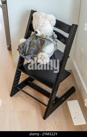 Un ours en peluche est assis sur une chaise haute. La chaise est noire et recouverte d'une couverture grise Banque D'Images