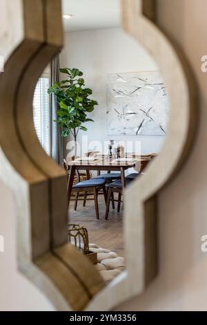 Un miroir avec une image d'une peinture abstraite blanche et noire sur le mur derrière. Le miroir reflète la salle à manger avec une table et des chaises Banque D'Images