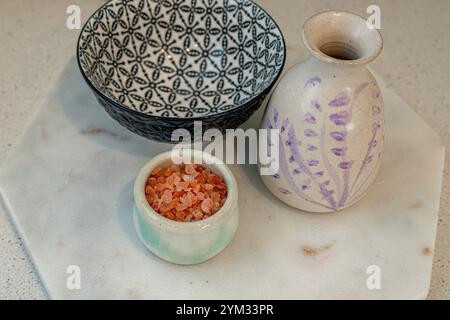 Un bol blanc avec un motif de fleur violette se trouve sur un plateau blanc. Un petit bol de sel repose sur le plateau Banque D'Images