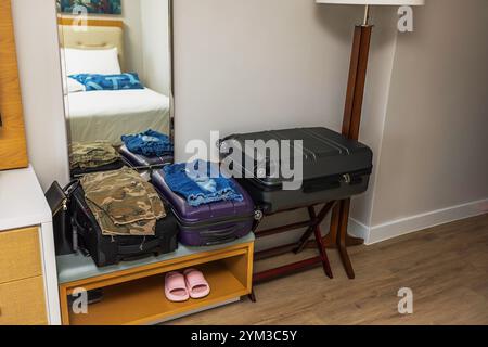 Valises emballées avec des vêtements pliés dans l'intérieur de la chambre d'hôtel avec miroir, plancher en bois et pantoufles roses sur l'étagère. Miami Beach. ÉTATS-UNIS. Banque D'Images