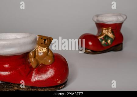 Décorations de bottes de père noël en céramique rouge avec petit ours en peluche et couronne de noël sur un fond lumineux Banque D'Images