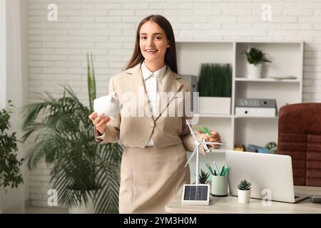 Ingénieur féminin avec tirelire et modèle d'éolienne sur table dans le bureau Banque D'Images