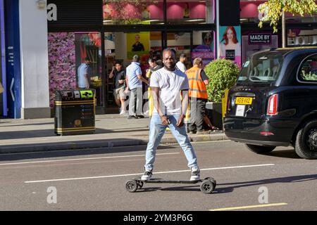 Londres, Angleterre, Royaume-Uni - 22 août 2023 : personne roulant sur une planche à roulettes dans la circulation au milieu d'Oxford Street dans le centre de Londres Banque D'Images