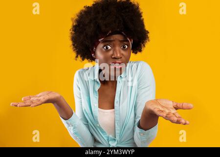 Perplexe, la African Lady hause dressant les épaules sur fond rose Banque D'Images