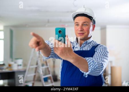 Foreman en salopette bleue prend une photo des locaux réparés à l'aide d'un téléphone portable Banque D'Images