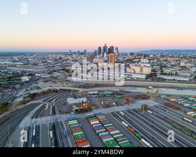 Vue aérienne de la skyline du centre-ville de Los Angeles au crépuscule, mettant en scène une cour de chemin de fer pour conteneurs d'expédition, la logistique industrielle et un paysage urbain au coucher du soleil Banque D'Images