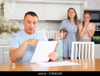 Un père mécontent lit attentivement les documents. Toute la famille est dans la peur en arrière-plan Banque D'Images