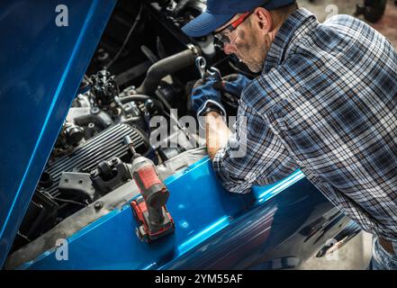 Un mécanicien travaille avec diligence sur un moteur à l'intérieur d'un atelier bien éclairé, en utilisant des outils et des compétences ciblées pour assurer des réparations appropriées dans la lumière de l'après-midi. Banque D'Images