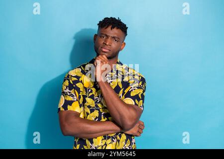 Jeune homme confiant dans une chemise florale élégante pose sur fond bleu vif avec une expression contemplative Banque D'Images