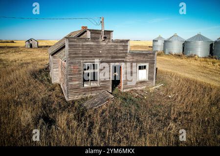 Une petite maison ancienne se trouve dans un champ de hautes herbes. La maison est dans un état de délabrement, avec quelques fenêtres arborées et une cheminée manquante. Le surro Banque D'Images