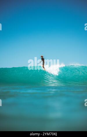 Un surfeur surfe sur une vague dans l'océan. Le surfeur porte une chemise noire et un short Banque D'Images