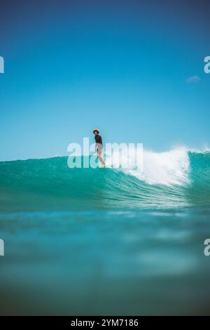 Un surfeur surfe sur une vague dans l'océan. Le surfeur porte une combinaison noire et une chemise noire Banque D'Images