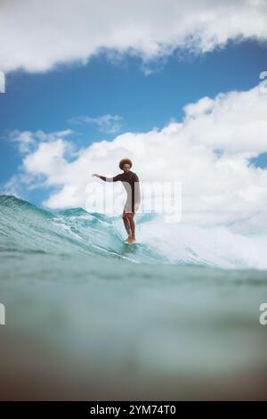 Un surfeur surfe sur une vague dans l'océan. Le surfeur porte une chemise noire et un short Banque D'Images